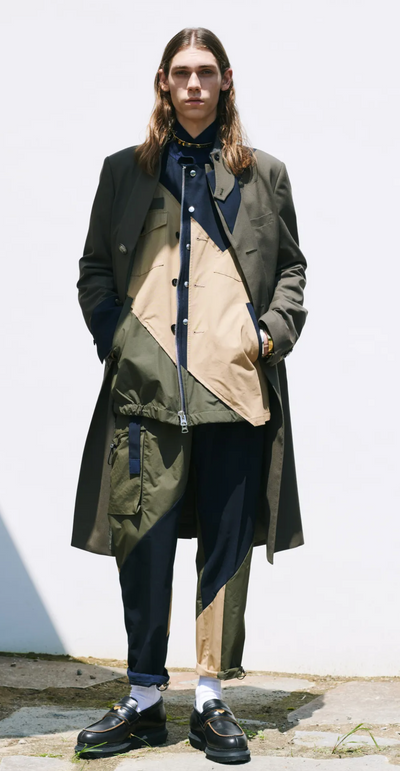 A man wearing a green and brown Sacai jacket with black loafers