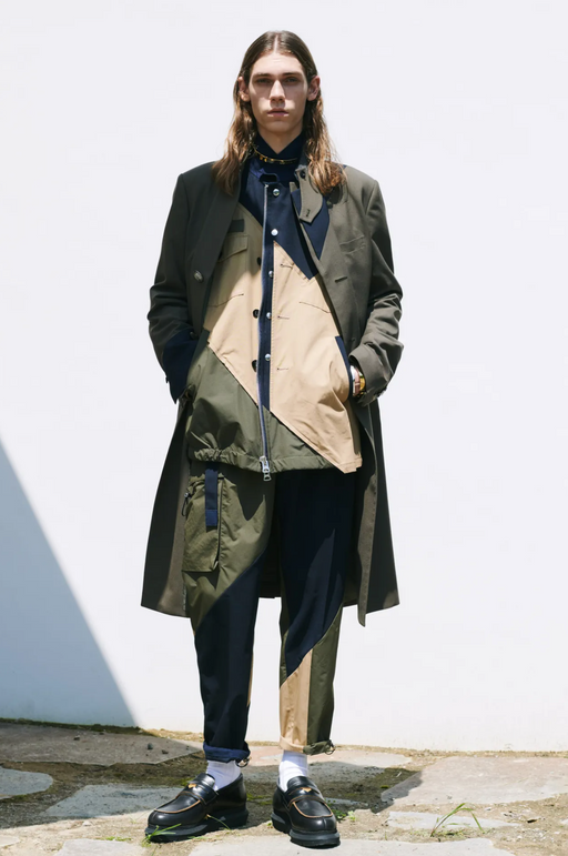 A man wearing a green and brown Sacai jacket with black loafers