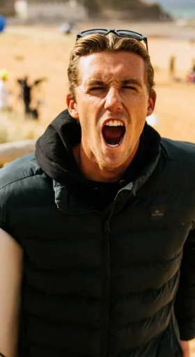A man wearing a a Rip Curl hoodie and jacket holding a surf board