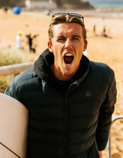 A man wearing a a Rip Curl hoodie and jacket holding a surf board