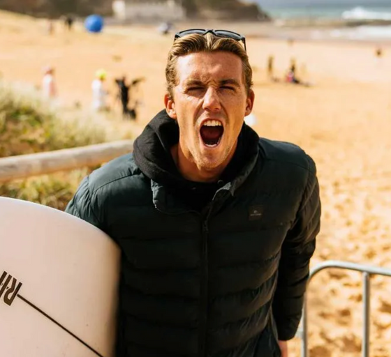 A man wearing a a Rip Curl hoodie and jacket holding a surf board