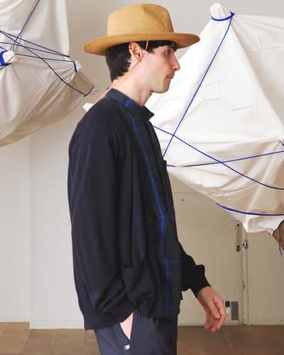 A man wearing a Nonnative navy blue sweater, blue button up and brown flat brimmed hat
