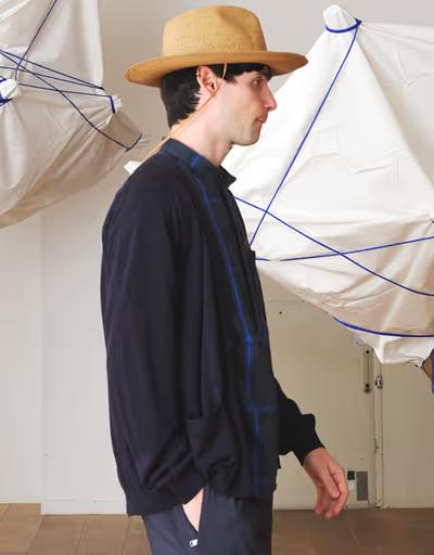 A man wearing a Nonnative navy blue sweater, blue button up and brown flat brimmed hat