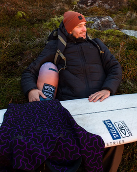 A man wearing a Billabong outfit sitting outside with a surf board