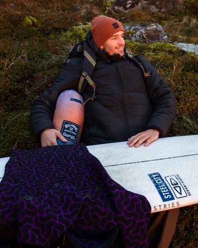 A man wearing a Billabong outfit sitting outside with a surf board