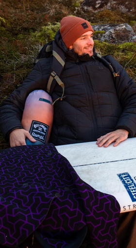 A man wearing a Billabong outfit sitting outside with a surf board