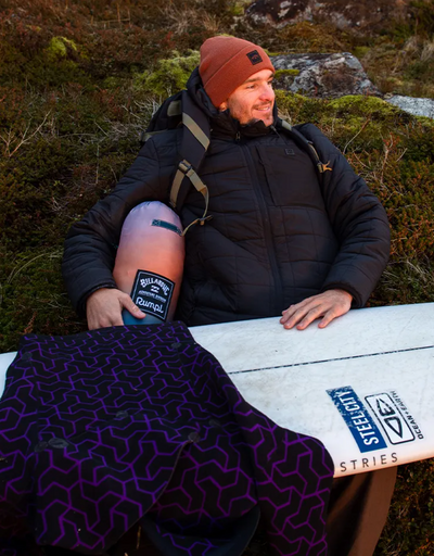 A man wearing a Billabong outfit sitting outside with a surf board