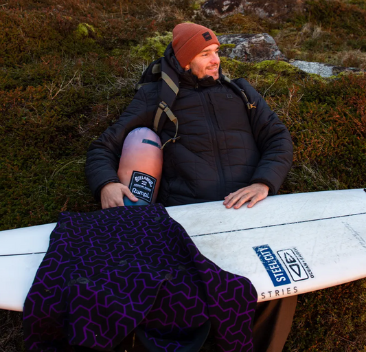 A man wearing a Billabong outfit sitting outside with a surf board