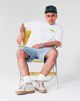 A man sitting and wearing a Bodega t-shirt with jean shorts