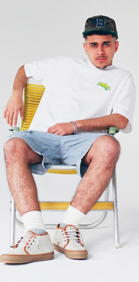 A man sitting and wearing a Bodega t-shirt with jean shorts