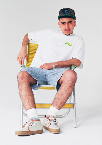 A man sitting and wearing a Bodega t-shirt with jean shorts