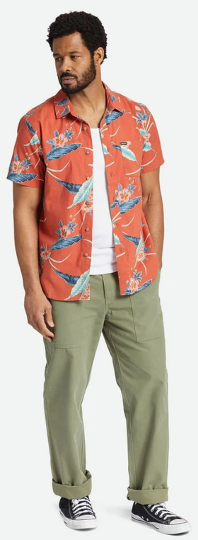 A man standing and wearing a Brixton outfit featuring an orange print button up, a white shirt and green pants