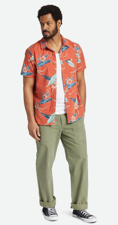 A man standing and wearing a Brixton outfit featuring an orange print button up, a white shirt and green pants