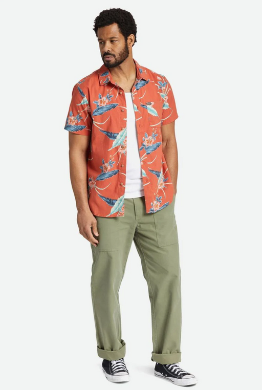 A man standing and wearing a Brixton outfit featuring an orange print button up, a white shirt and green pants