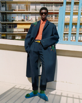 A man wearing a fashionable lacoste suit with flower embroidery on it and blue sandals