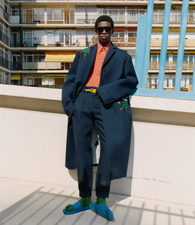 A man wearing a fashionable lacoste suit with flower embroidery on it and blue sandals