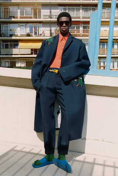 A man wearing a fashionable lacoste suit with flower embroidery on it and blue sandals