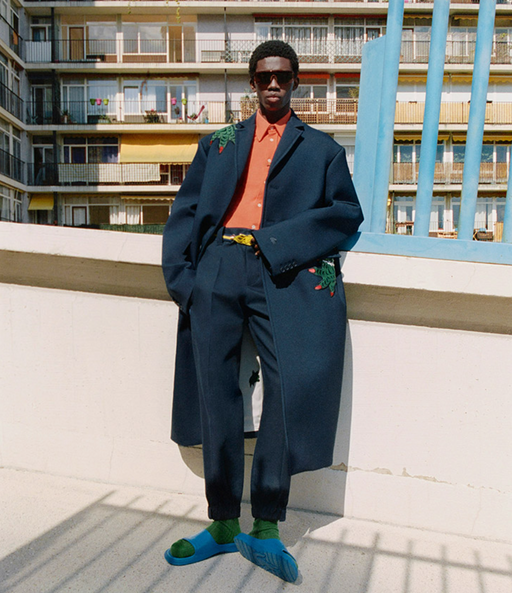 A man wearing a fashionable lacoste suit with flower embroidery on it and blue sandals
