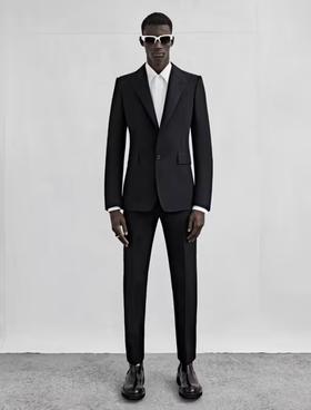 A man wearing a black Alexander McQueen suit with black and white sunglasses