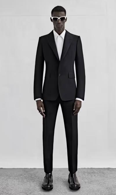 A man wearing a black Alexander McQueen suit with black and white sunglasses