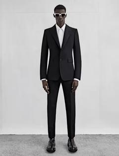 A man wearing a black Alexander McQueen suit with black and white sunglasses