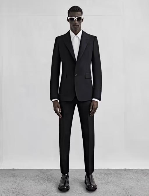 A man wearing a black Alexander McQueen suit with black and white sunglasses