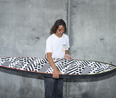 A man holding a surf board wearing a Vissla white t-shirt