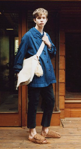 A man wearing a Visvim denim jacket, beige carryall, dark pants and brown slippers