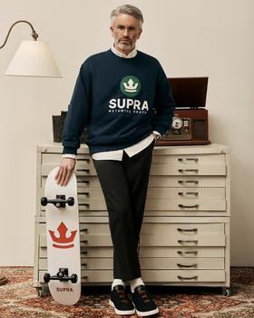 A man wearing a Supra crewneck sweater with a white button shirt underneath