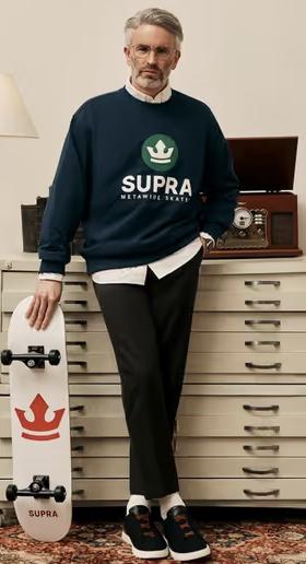 A man wearing a Supra crewneck sweater with a white button shirt underneath