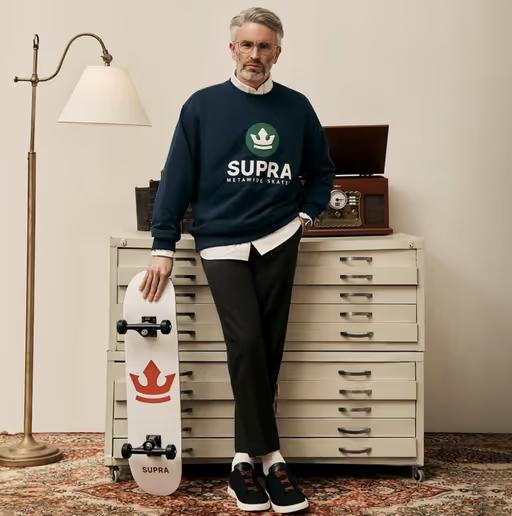 A man wearing a Supra crewneck sweater with a white button shirt underneath