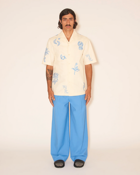 A man wearing a Nanushka button up yellow shirt and blue pants