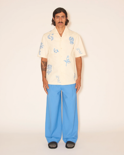 A man wearing a Nanushka button up yellow shirt and blue pants