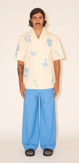 A man wearing a Nanushka button up yellow shirt and blue pants