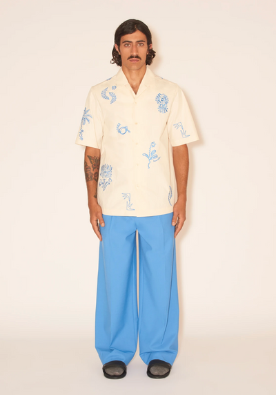 A man wearing a Nanushka button up yellow shirt and blue pants