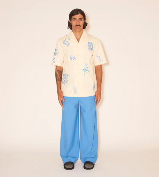 A man wearing a Nanushka button up yellow shirt and blue pants