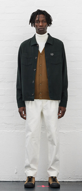 A man wearing a Fred Perry outfit featuring a turtle neck, navy blue jacket and white pants
