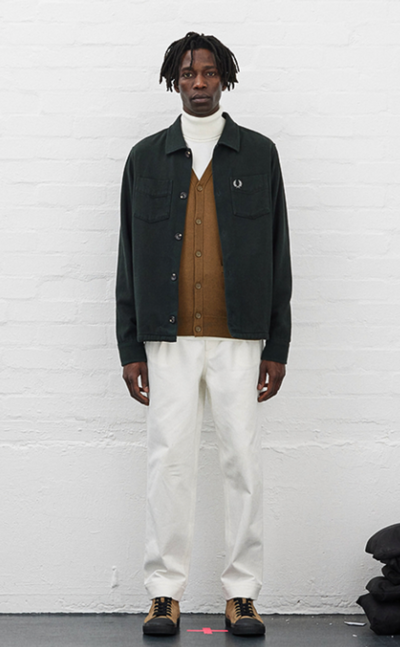 A man wearing a Fred Perry outfit featuring a turtle neck, navy blue jacket and white pants