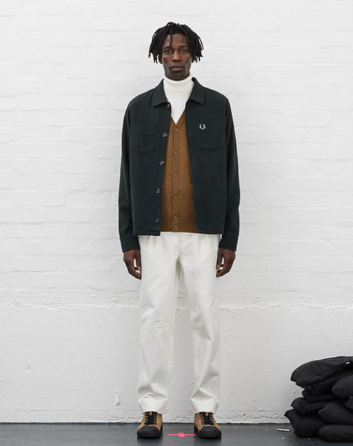 A man wearing a Fred Perry outfit featuring a turtle neck, navy blue jacket and white pants