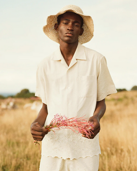 A man wearing a CMMN SWDN cream button up with a farmers hat