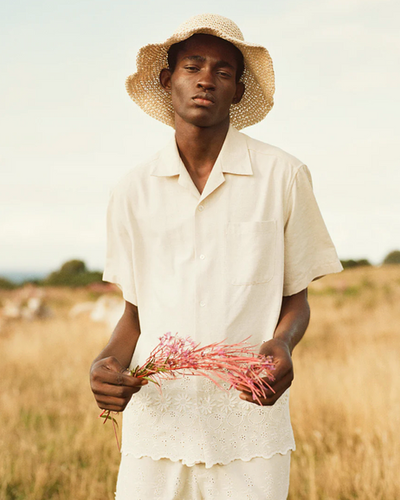 A man wearing a CMMN SWDN cream button up with a farmers hat