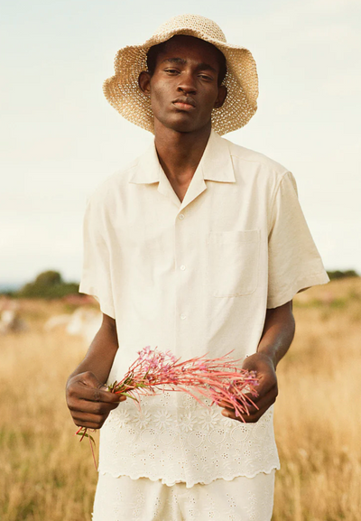 A man wearing a CMMN SWDN cream button up with a farmers hat
