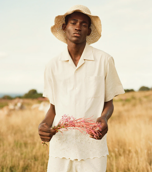 A man wearing a CMMN SWDN cream button up with a farmers hat