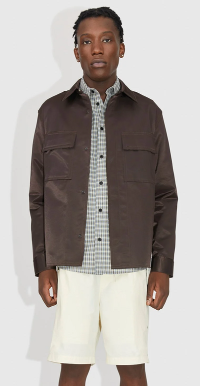 A man wearing a brown Wood Wood jacket with a checkered button up and beige shorts