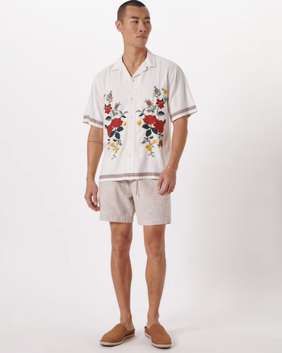 A man wearing a floral Abercrombie & Fitch white shirt and light grey shorts with brown shoes