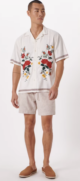 A man wearing a floral Abercrombie & Fitch white shirt and light grey shorts with brown shoes