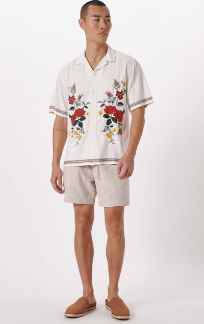 A man wearing a floral Abercrombie & Fitch white shirt and light grey shorts with brown shoes