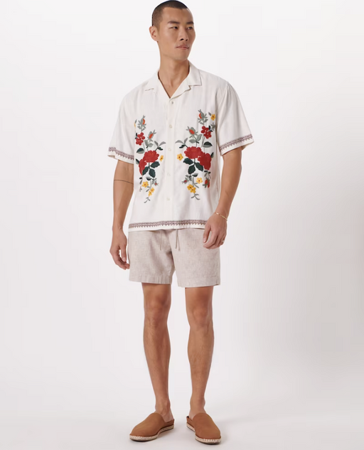 A man wearing a floral Abercrombie & Fitch white shirt and light grey shorts with brown shoes