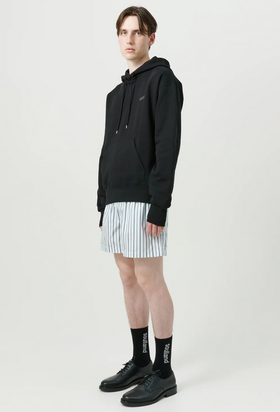 A man wearing a soulland hoodie with short striped shorts and black shoes
