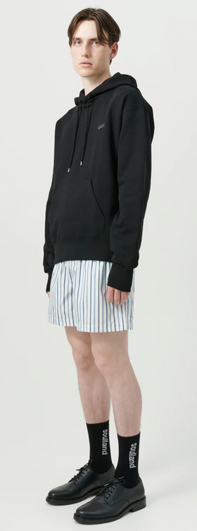 A man wearing a soulland hoodie with short striped shorts and black shoes